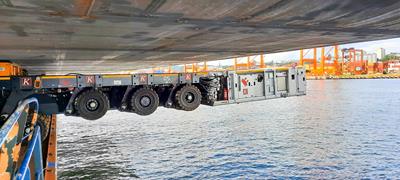 À quelques mètres de là, le convoi Cometto SPMT de l'entreprise allemande Krebs Korrosionsschutz GmbH dépasse par-dessus le bord d’une barge.