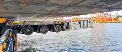 À quelques mètres de là, le convoi Cometto SPMT de l'entreprise allemande Krebs Korrosionsschutz GmbH dépasse par-dessus le bord d’une barge.